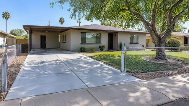 Freshly replaced concrete driveway at a modest 1960s ranch-style block home in west Phoenix with a chain-link fence, a shade tree and a clean front yard