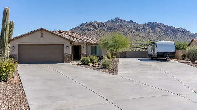 Concrete RV pad and wide driveway at a single-story home in south Phoenix with the rugged ridgeline of South Mountain behind under a clear sky